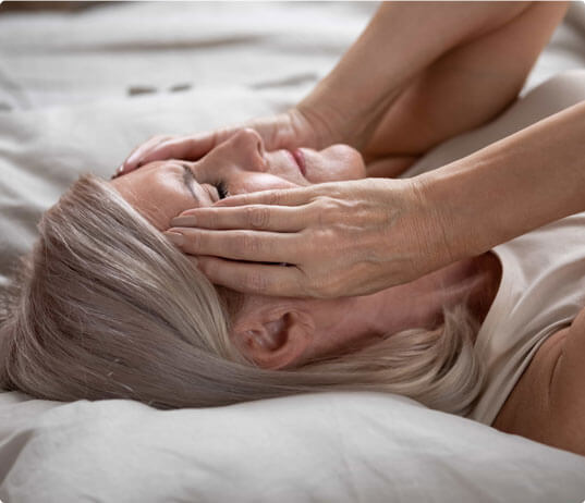 Woman lying down touching her head in need of hormone replacement therapy in Tucson, AZ